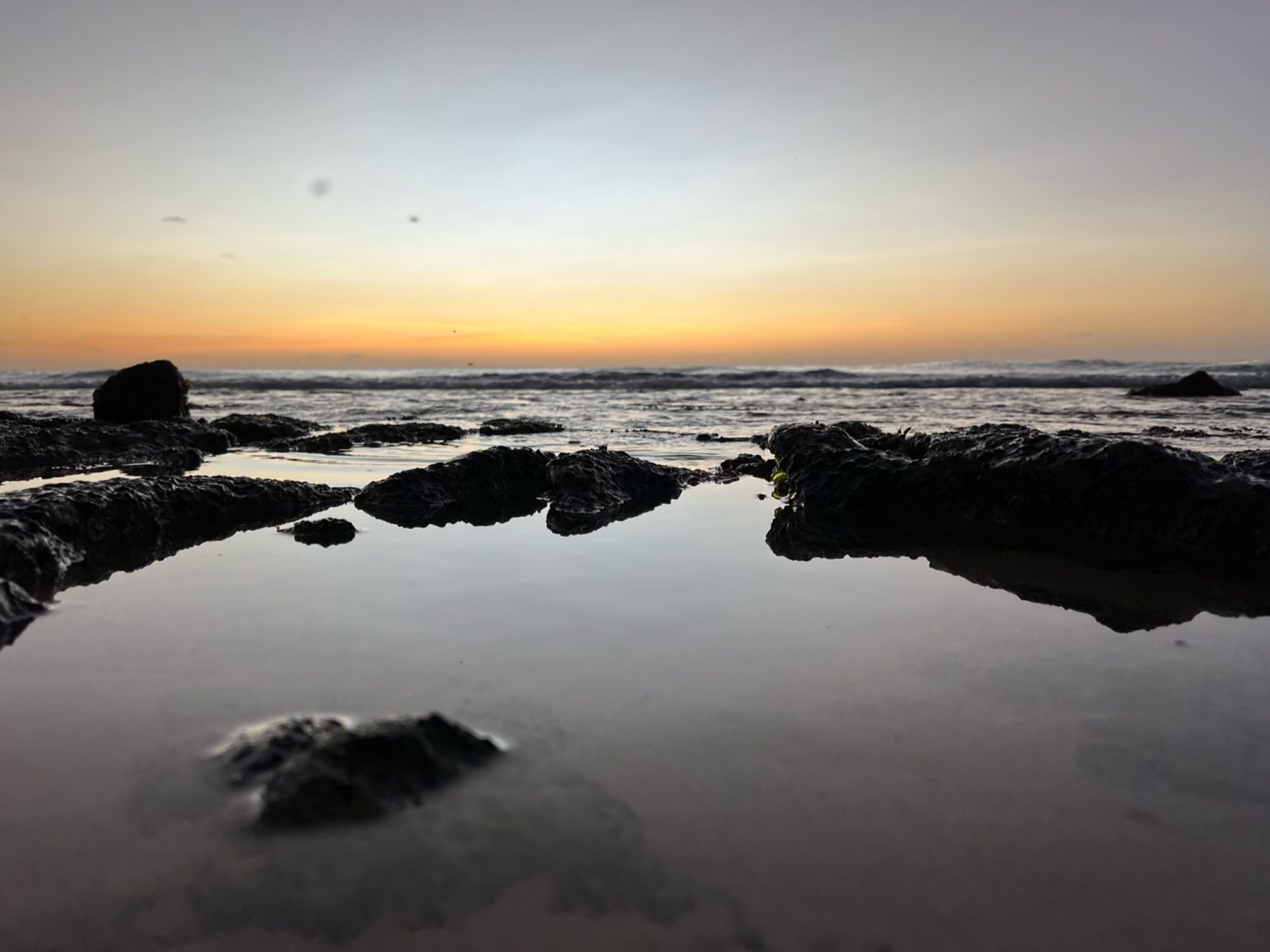 Sunset over a rocky shoreline, the sky glowing above the sea.