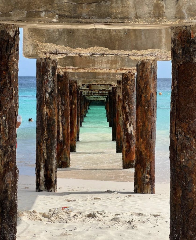 View beneath a weathered pier looking out to turquoise water.