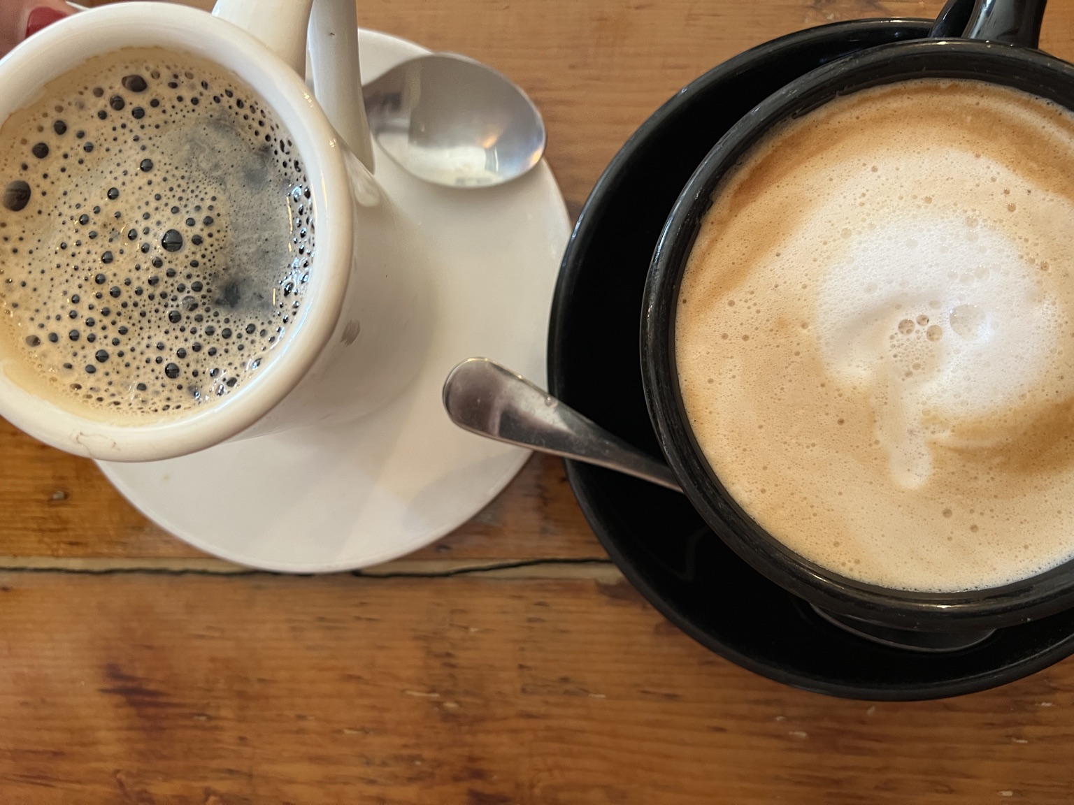 Two coffees, a black coffee and a flat white, on a wooden cafe table.
