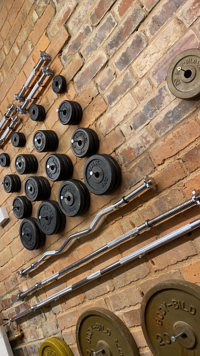 Weight plates and barbells racked on a brick gym wall.